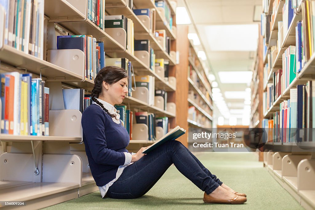 Woman reading book sitting against bookshelves