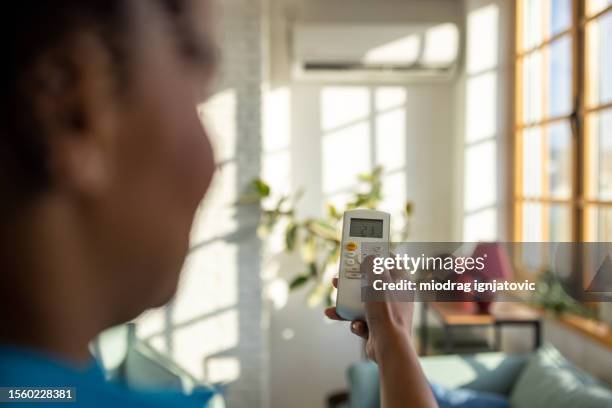 woman turning on an air conditioning unit in her living room - remote controlled stock pictures, royalty-free photos & images