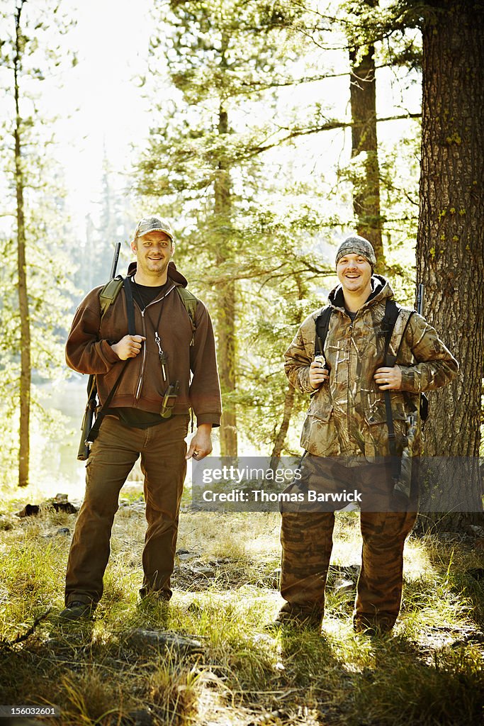 Two male hunters standing in woods with rifles