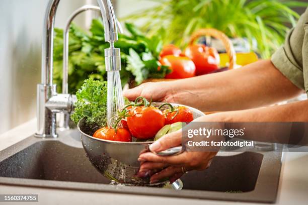 frau hält ein sieb voller frischem gemüse unter fließendem wasser in der küchenspüle - waschen stock-fotos und bilder