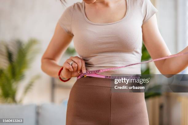 mujer joven midiendo su cintura en casa - preocupación por el cuerpo fotografías e imágenes de stock