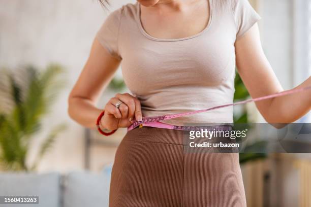 young woman measuring her waist at home - centimetre stock pictures, royalty-free photos & images
