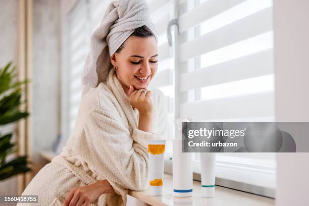 young woman with blank beauty products standing next to a window - robe tube stock pictures, royalty-free photos & images