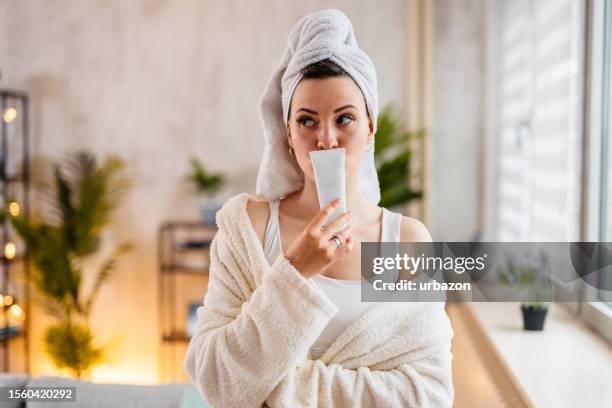 young woman holding up a blank moisturizer product in the living room - robe tube stock pictures, royalty-free photos & images