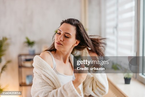 Mujer joven rociando un producto para el cabello en su cabello en la sala de estar Mujer joven rociando un producto para el cabello en su cabello en la sala de estar