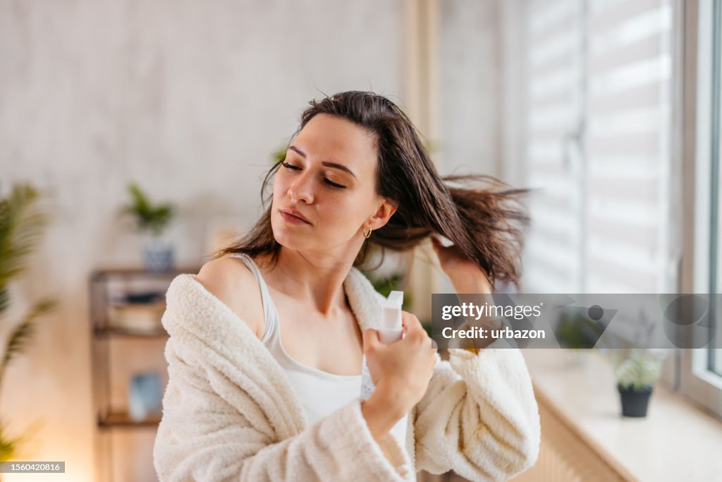 Jeune femme pulvérisant un produit capillaire sur ses cheveux dans le salon