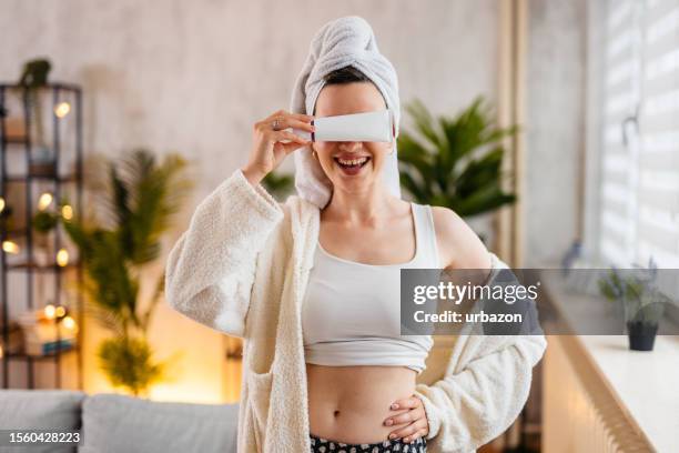 young woman holding up a blank moisturizer product in the living room - robe tube stock pictures, royalty-free photos & images