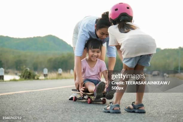 mother teaching her daughter how to skateboard in the park,thailand - mother and daughter riding on skateboard in park stock pictures, royalty-free photos & images