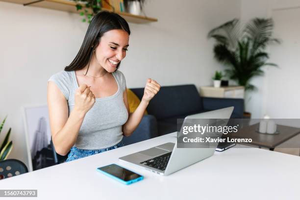 ecstatic young beautiful millennial woman celebrating success looking at laptop computer screen at home. female receiving good news on email. - loto photos et images de collection