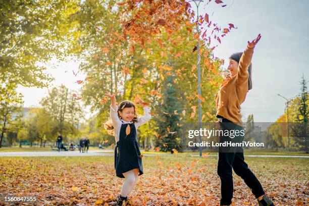 mother and daughter throwing autumn leaves in the air - oktober stockfoto's en -beelden