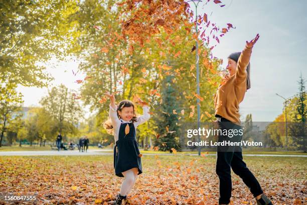 mother and daughter throwing autumn leaves in the air - oktober stock pictures, royalty-free photos & images