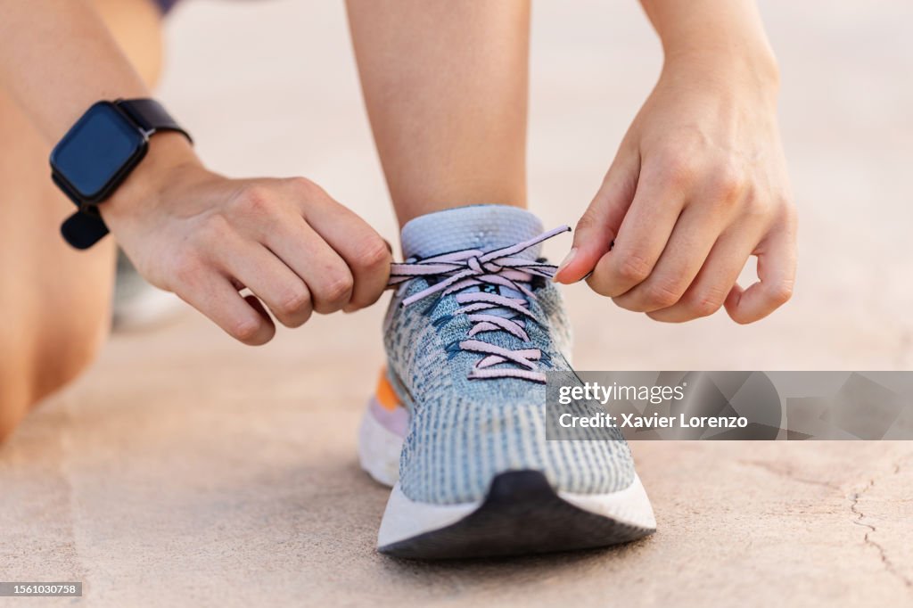 Close-up view of female jogger hands tying laces of her sport shoes before running exercise routine. Motivation, healthy lifestyle and fitness concept.