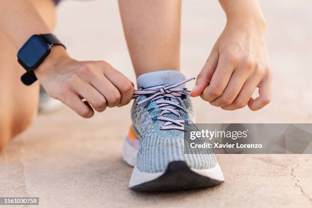 close-up view of female jogger hands tying laces of her sport shoes before running exercise routine. motivation, healthy lifestyle and fitness concept. - vastgebonden stockfoto's en -beelden