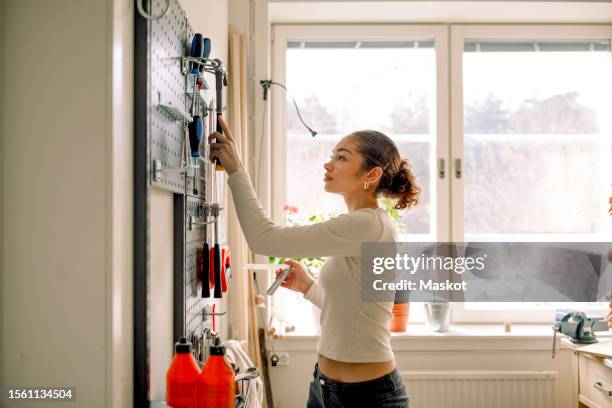 side view of female teenage student selecting tools from pegboard during carpentry class - sólo chicas adolescentes fotografías e imágenes de stock