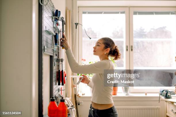 side view of female teenage student selecting tools from pegboard during carpentry class - only teenage girls stock pictures, royalty-free photos & images