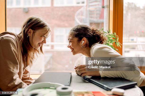 smiling female teenage friends gossiping with each other at high school - in ear headphones stock pictures, royalty-free photos & images