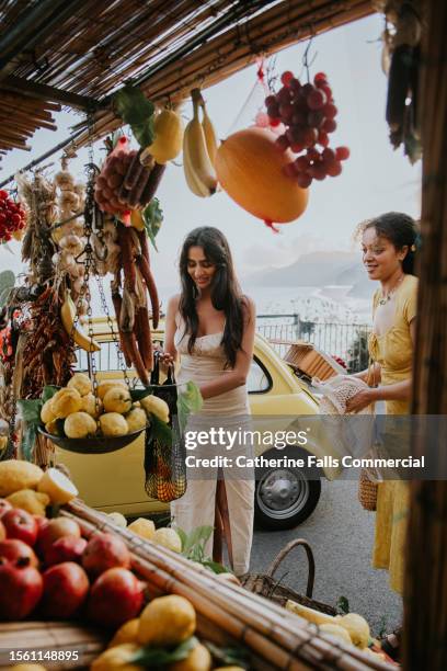 two young woman buy fruit from a fruit stall - verschiedene kulturen stock-fotos und bilder