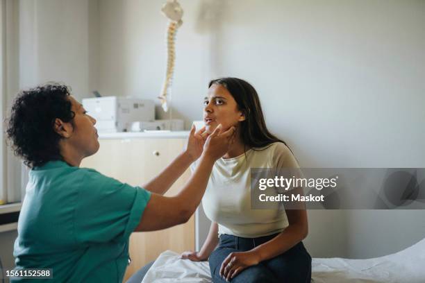 female physician checking throat of young woman sitting in clinic - thyroid exam stock pictures, royalty-free photos & images