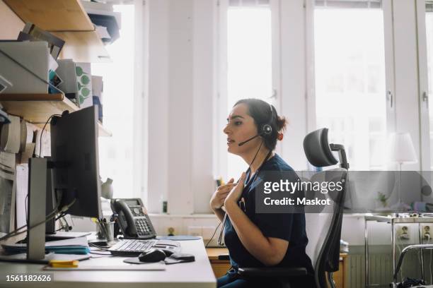 side view of mature female nurse doing video call while sitting on chair in clinic - desktop computer stock pictures, royalty-free photos & images