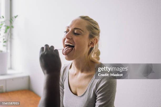 doctor examining female patient with mouth open in clinic - sticking out tongue stock pictures, royalty-free photos & images