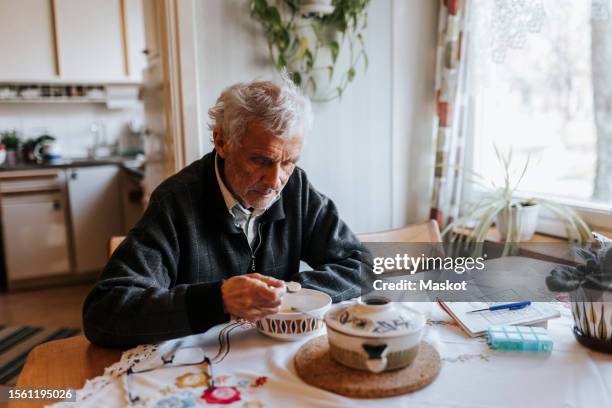 senior man eating breakfast while sitting at dining table in home - einzelner senior stock-fotos und bilder