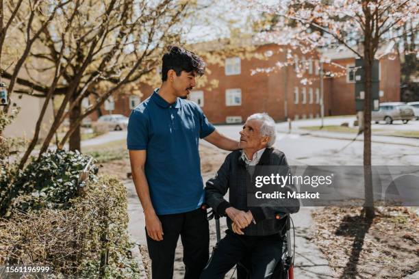 male caregiver with hand on shoulder of senior man sitting on walker - social rehabilitation centre stock pictures, royalty-free photos & images