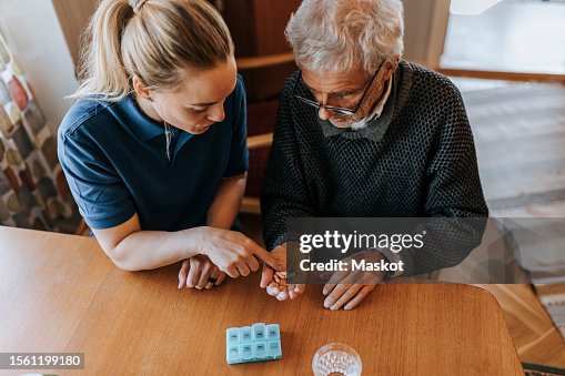 High angle view of female caregiver explaining medicine dose to senior man at home High angle view of female caregiver explaining medicine dose to senior man at home