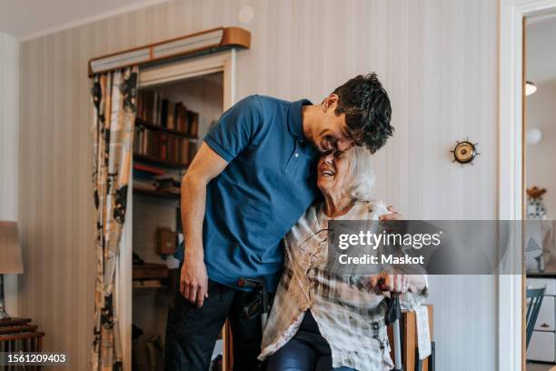 happy male caregiver embracing senior woman at home - asistencia de la comunidad fotografías e imágenes de stock