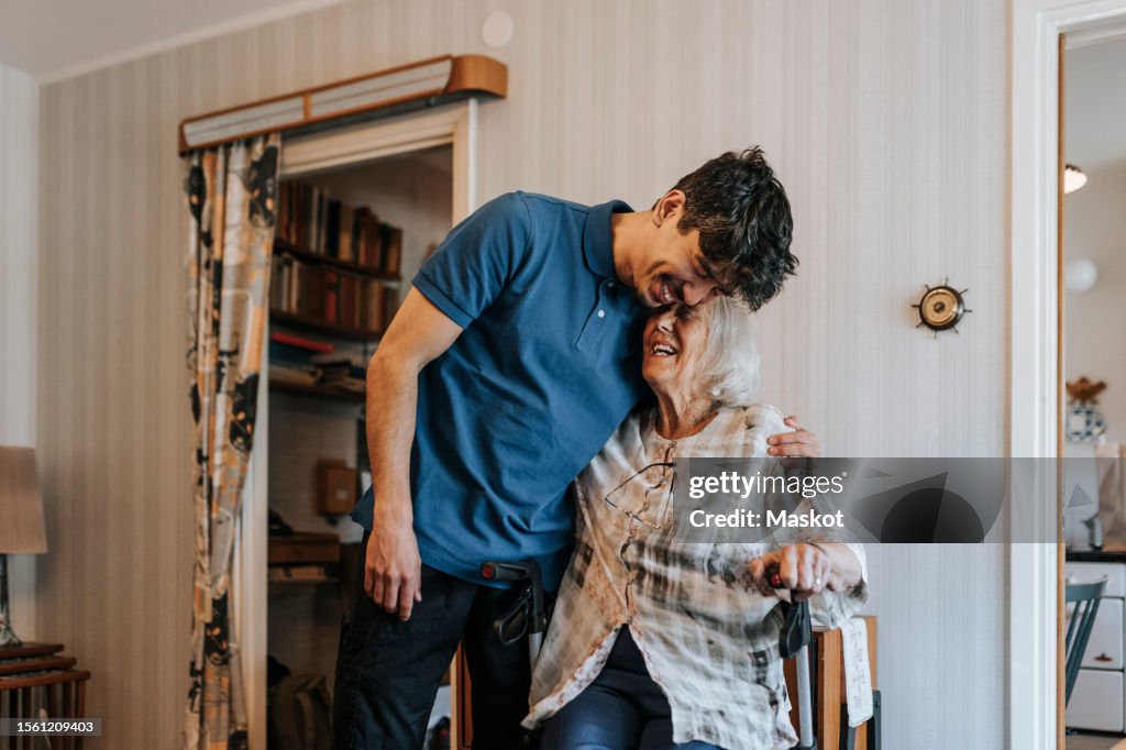 Happy male caregiver embracing senior woman at home
