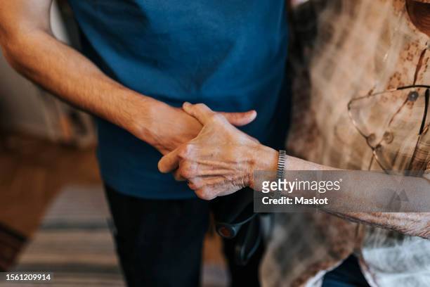 midsection of male healthcare worker holding hand of senior woman at home - old woman young man stock pictures, royalty-free photos & images
