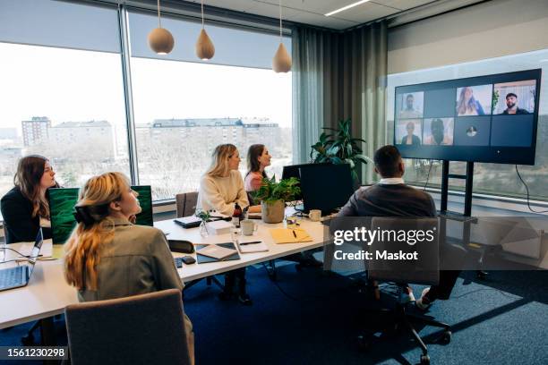 male and female business colleagues looking at tv screen with video conference display in coworking office - conference call stock pictures, royalty-free photos & images