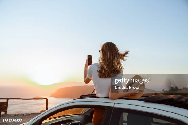 young woman taking a photo of the sunset - solo reizen stockfoto's en -beelden