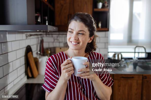 morning bliss: donna che assapora il caffè con un sorriso - woman smile kitchen foto e immagini stock