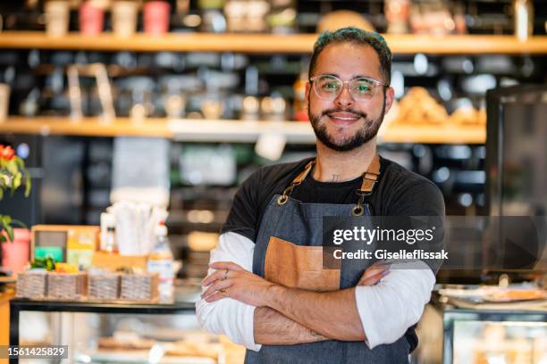 lächelnder junger barista, der vor einer café-theke steht - gastronomieberuf stock-fotos und bilder