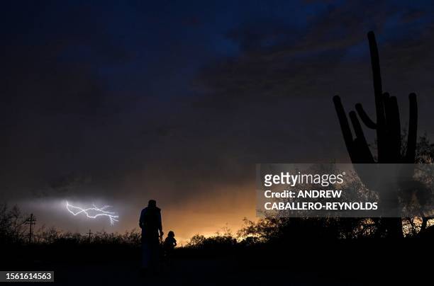 Family walks past Saguaro cacti as lightning forms in the distance in Tucson, Arizona, July 28, 2023.