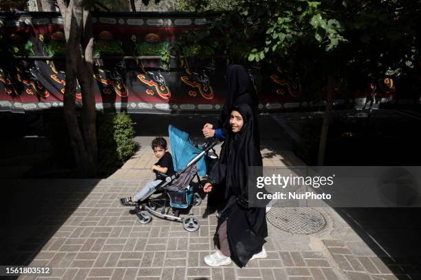 Veiled Iranian woman and her young veiled daughter walk past a religious flag in the city of Isfahan, on Ashura on the tenth day of the Muslim holy...