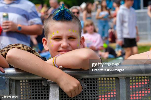 Young boy with blue and green spiked Mohican style hair leaning on the barrier watches North American performance art comedy disco duo from...
