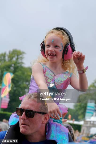 Young girl wearing a fairy dress and ear defenders, sitting on a man's shoulder watches North American performance art comedy disco duo from...