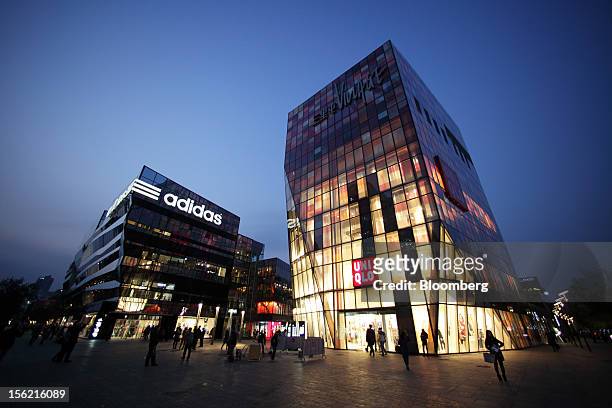 An Adidas AG store, left, and a Fast Retailing Co. Uniqlo store stand at night in the Sanlitun area of Beijing, China, on Friday, Nov. 9, 2012....