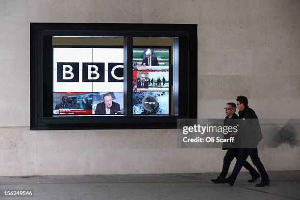Men walk past a bank of television screens displaying BBC channels in the BBC headquarters at New Broadcasting House on November 12, 2012 in London,...