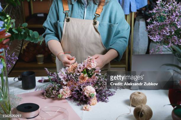 a young woman, a professional florist takes care of flowers in a cozy flower shop and collects beautiful modern bouquets. floristry, small business. the concept of retail, private business, startup. a seller in a flower shop creates a creative bouquet. - entrepreneur stockfoto's en -beelden