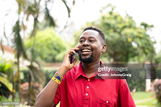 outdoor portrait of laughing african man using smart phone - red shirt stock pictures, royalty-free photos & images