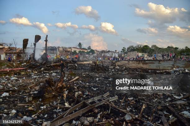 Thai police, rescue crew and locals gather around destroyed homes after an explosion ripped through a firework warehouse, killing nine people and...