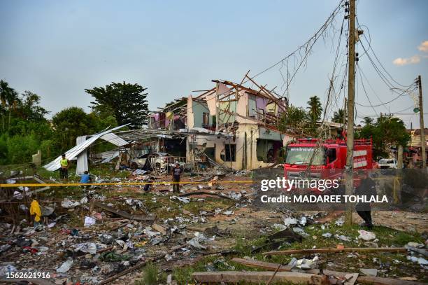 Thai police, rescue crew and locals gather around destroyed homes after an explosion ripped through a firework warehouse, killing nine people and...