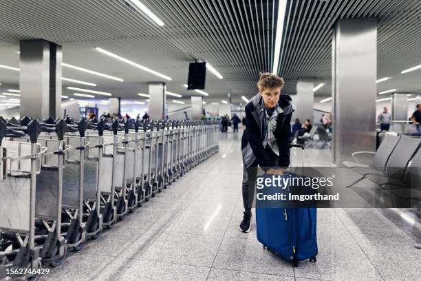 teenage boy pushing suitcase at the airport baggage claim - packed suitcase stock pictures, royalty-free photos & images