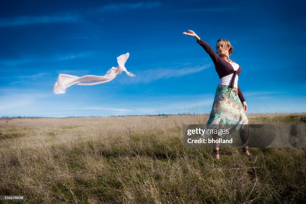 Young Woman Standing in Field Lettting Wind Take Scarf