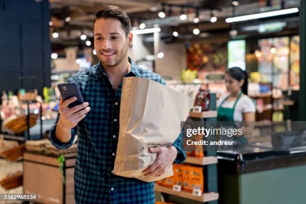 homme quittant le supermarché avec un sac de courses et vérifiant le solde de son compte - sachet en papier photos et images de collection