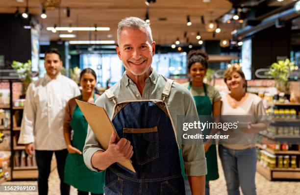 happy business owner with a group of employees at the supermarket - cornershop stockfoto's en -beelden