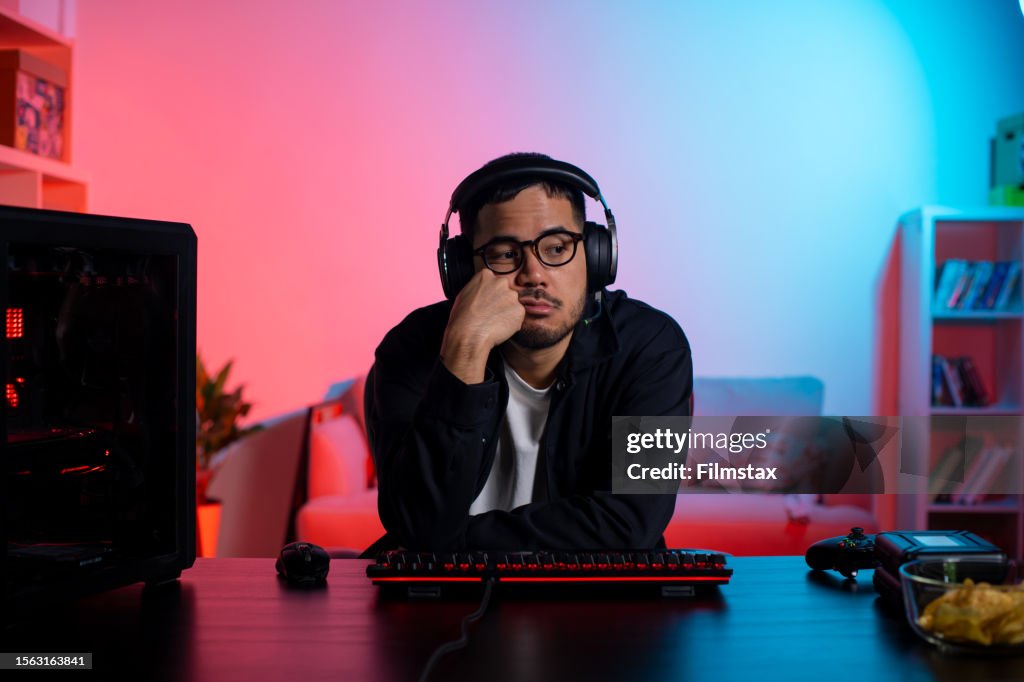 Young Asian man playing a video game feeling bored and disappointed at the game