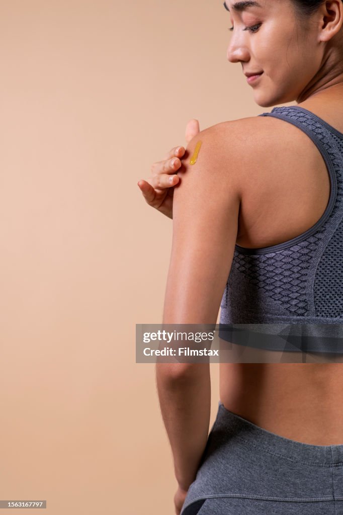 Attractive Young Asian Woman In Sports Bras Applying Moisturizer On Her  Shoulder On Beige Background High-Res Stock Photo - Getty Images